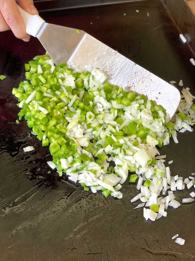 diced green pepper and onions cooking on a griddle