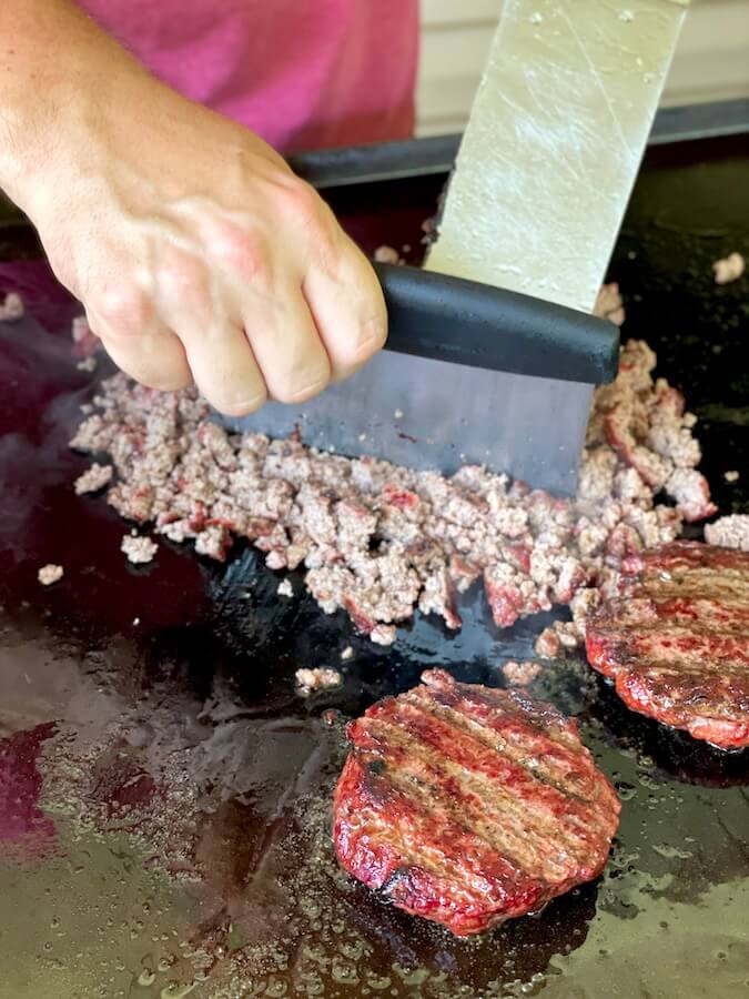chopping smoked beef patties on a griddle for sloppy joes