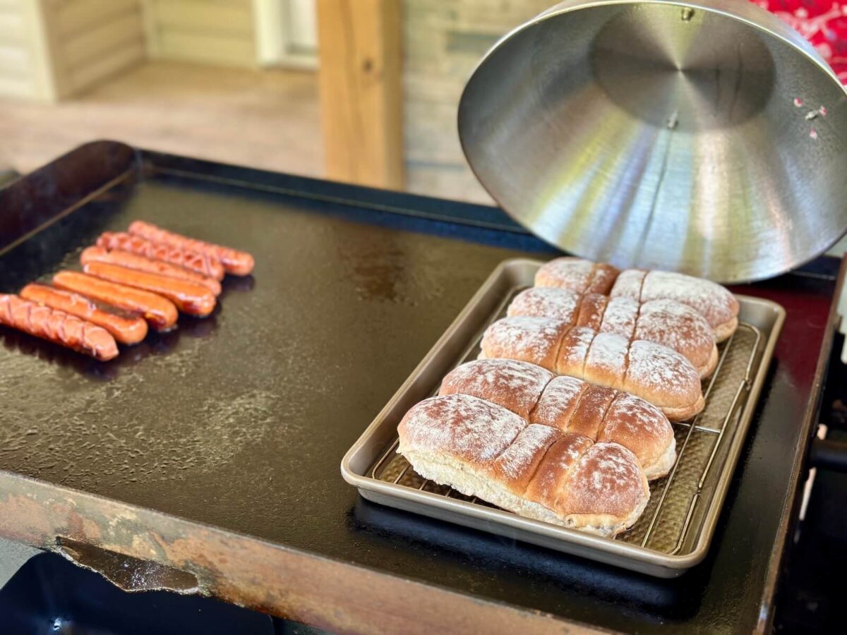using a Blackstone griddle to cook hot dogs on one side and steam buns on a sheet tray on the other side