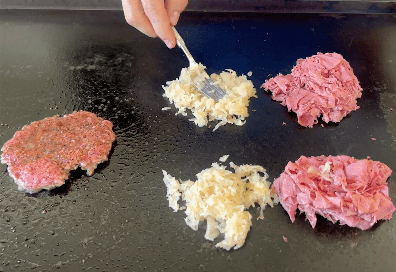 cooking pastrami, corned beef, and sauerkraut on a griddle