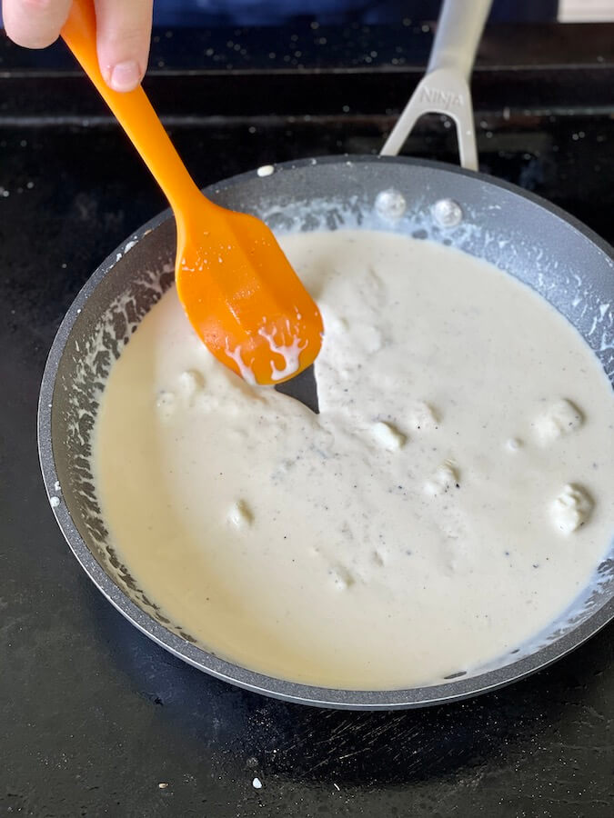 making a garlic cheesy cream sauce in a skillet