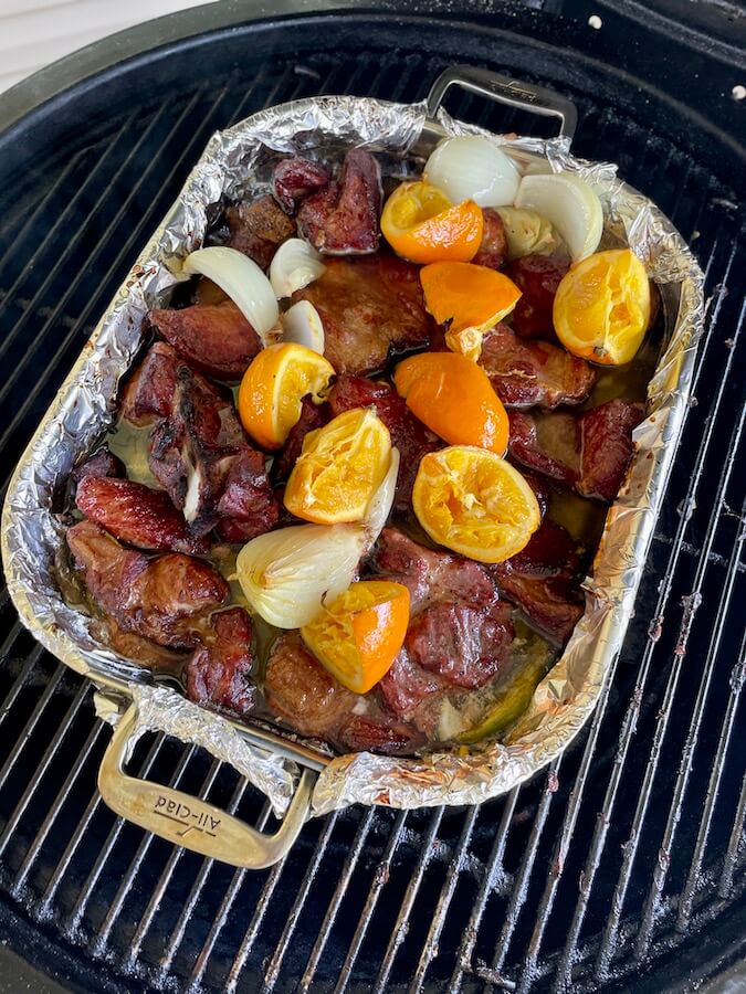 smoking pork carnitas in a pan with oranges, lard, coca cola, and onions