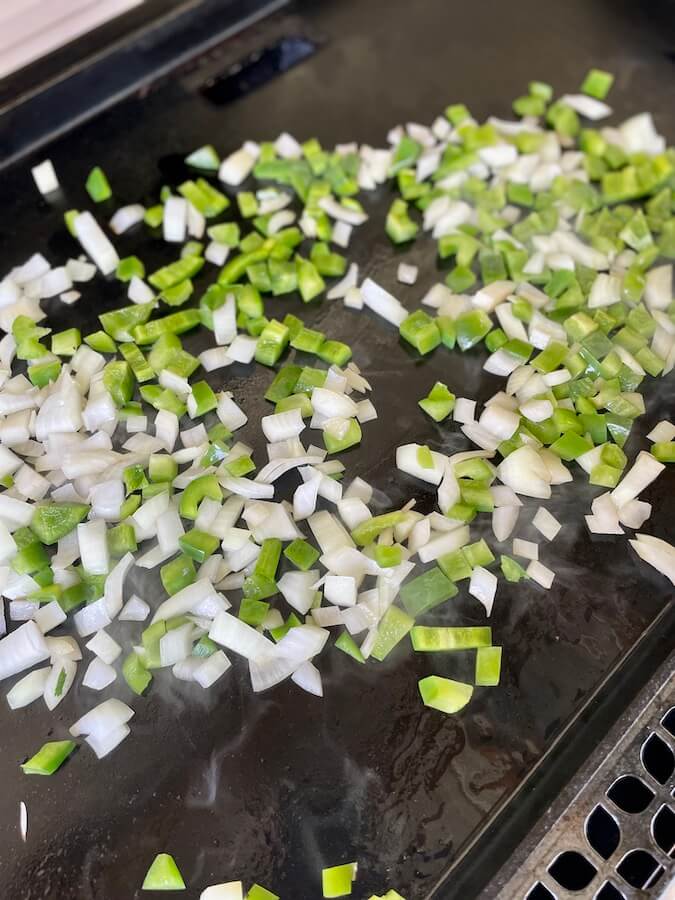 diced onions and peppers cooking on a griddle