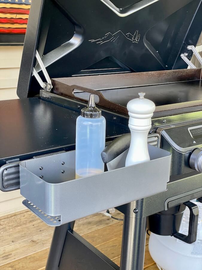 pepper mill and oil bottle in a storage basket attachment on the Traeger griddle