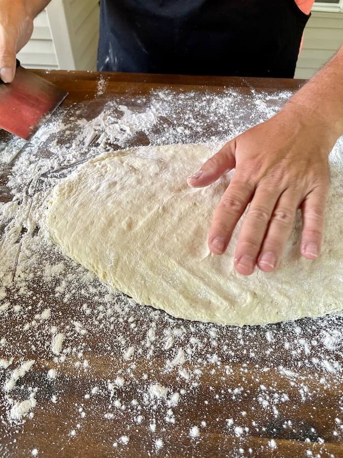 patting out english muffin dough on a floured cutting board