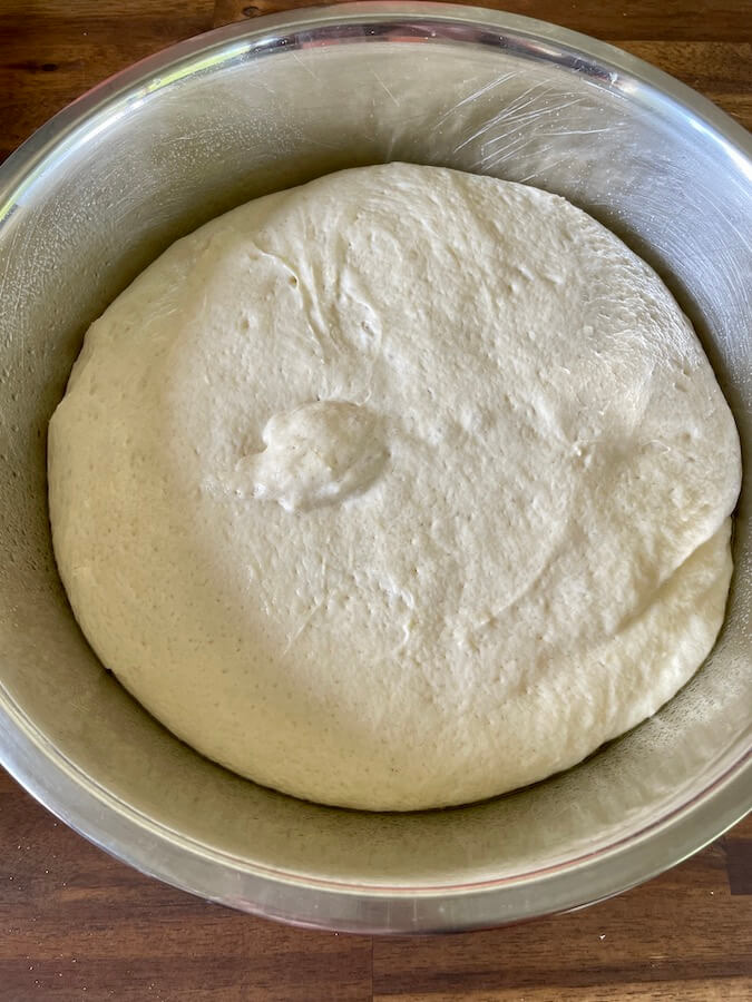 english muffin dough proofing in a metal bowl
