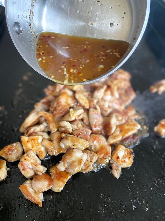 adding homemade orange chicken sauce to cooked chicken on a griddle