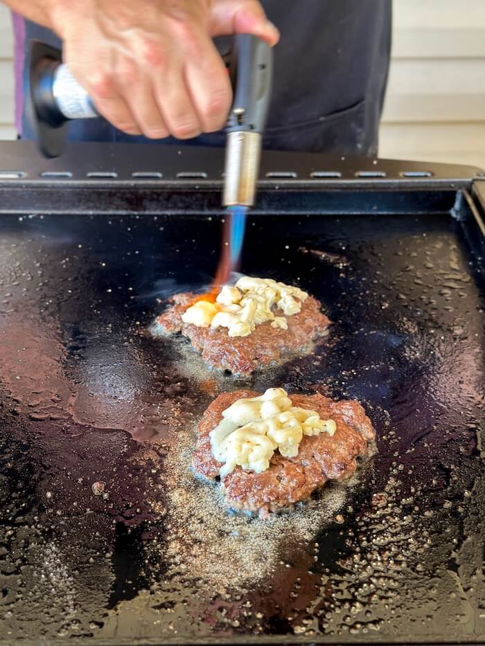 using a small torch to melt cheese on a bone marrow burger