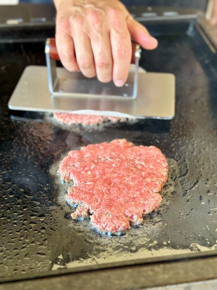 smashing burgers on a griddle
