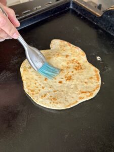 brushing naan bread with melted butter on the griddle