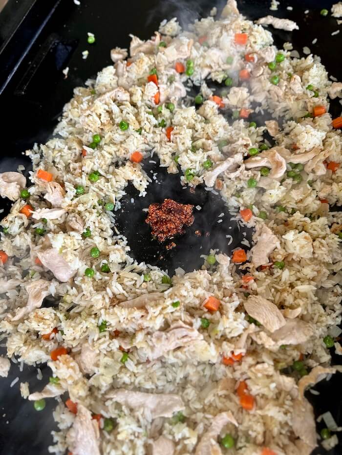 mixing chili sauce into chicken fried rice on the Blackstone griddle
