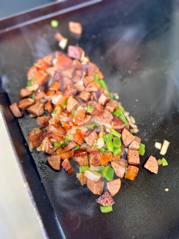 sausage, peppers, and onions cooking on a Blackstone griddle
