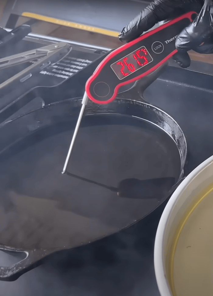 using an instant read thermometer to check oil temperature in a cast iron skillet on the griddle