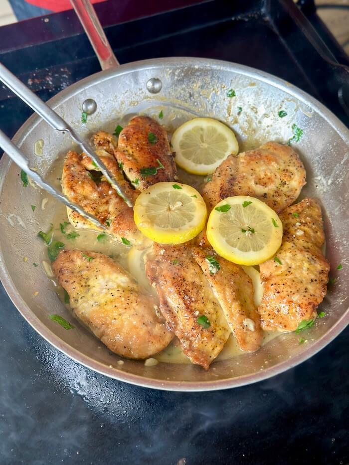 cooking lemon pepper chicken in a skillet on the griddle