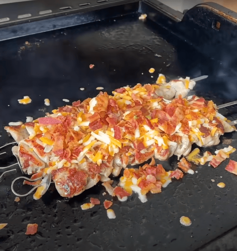 chicken kabobs with cheese and bacon cooking on a griddle