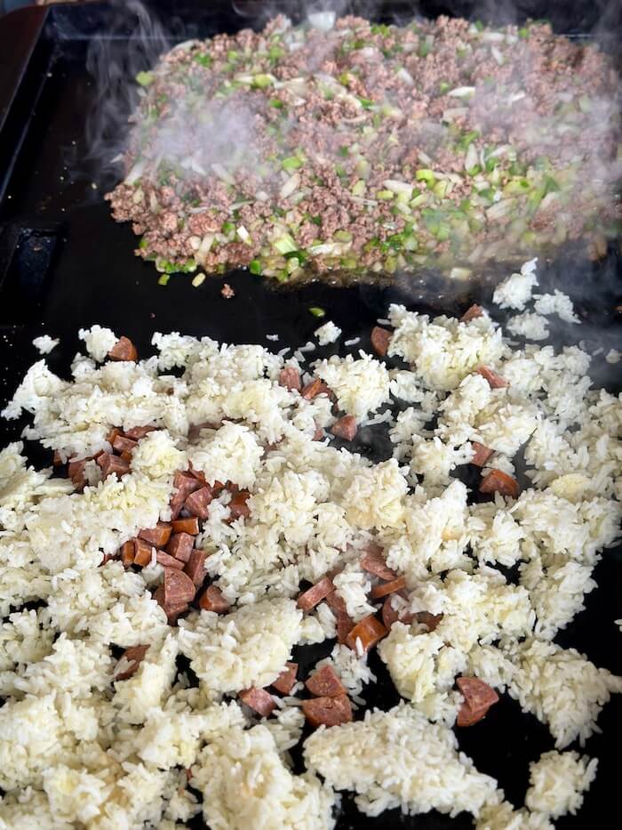 white rice, sausage, ground beef, and vegetables cooking on a griddle