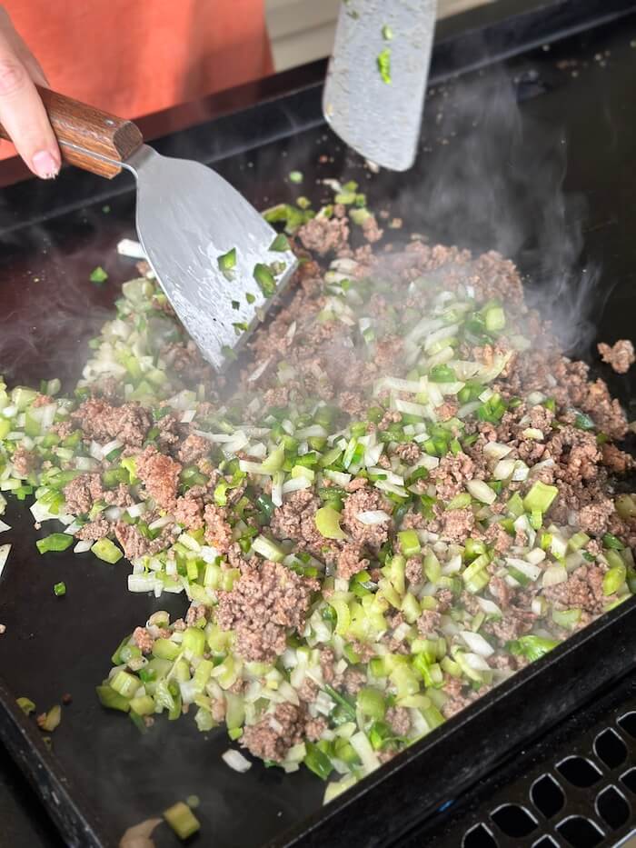 cooking ground beef and diced vegetables on the griddle