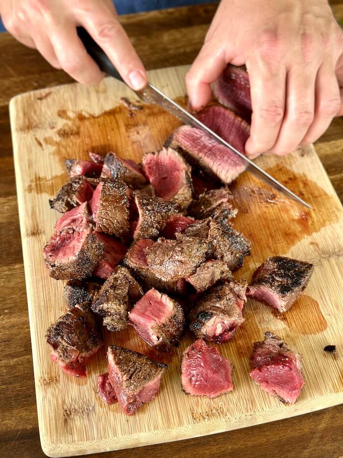 cutting seared steak into bite-sized cubes
