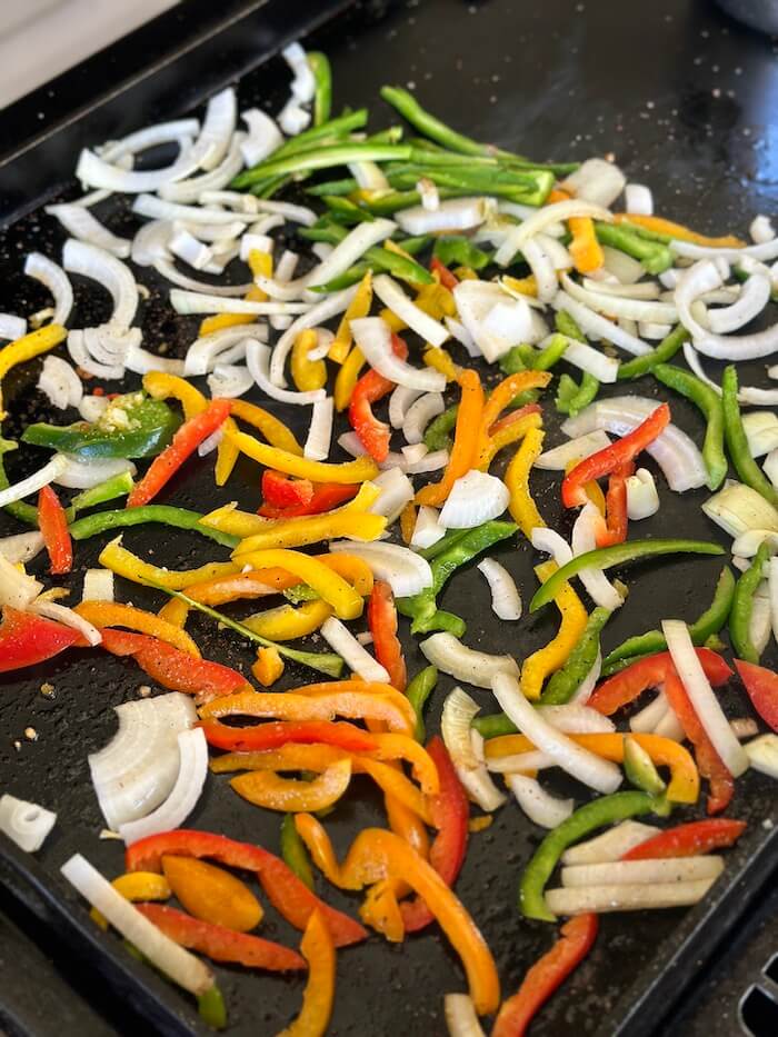 cooking sliced bell peppers and onions on the griddle