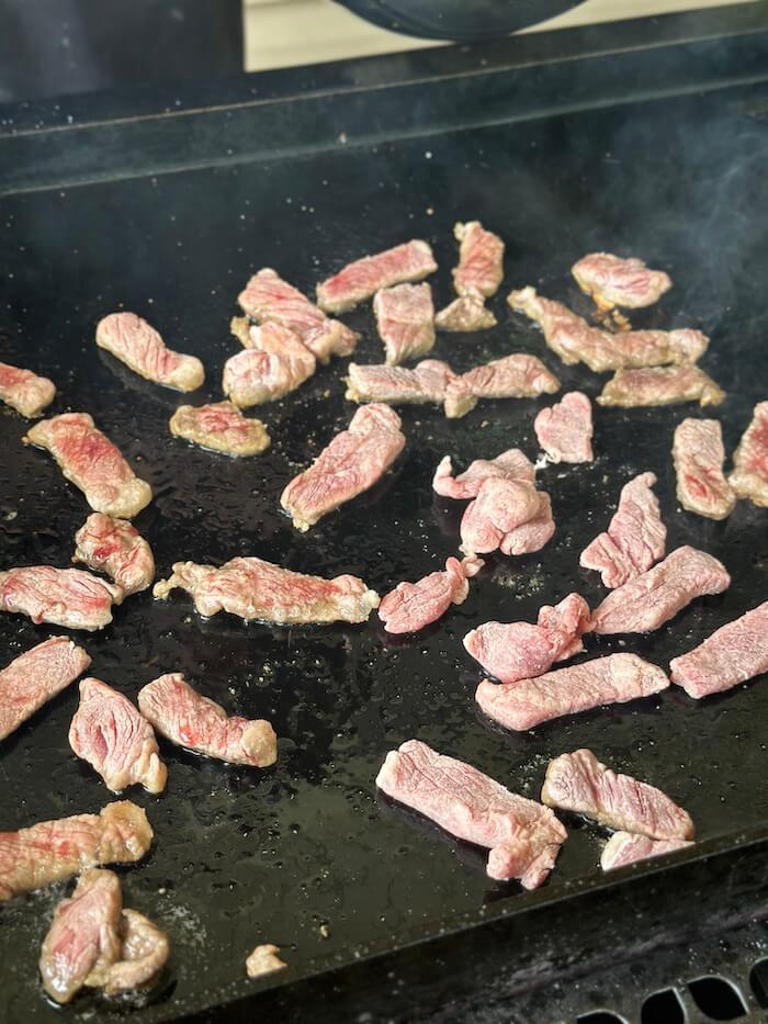 strips of steak cooking on a griddle