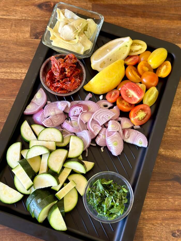 cut up vegetables including zucchini, shallot, and grape tomatoes