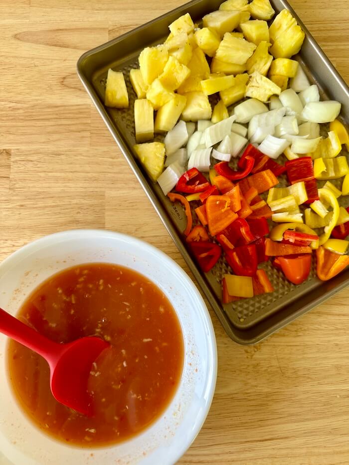 sweet and sour chicken sauce in a bowl and cut pineapple and bell peppers