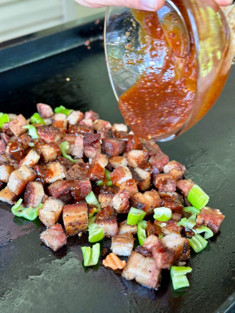 adding sauce to crispy pork belly on a griddle