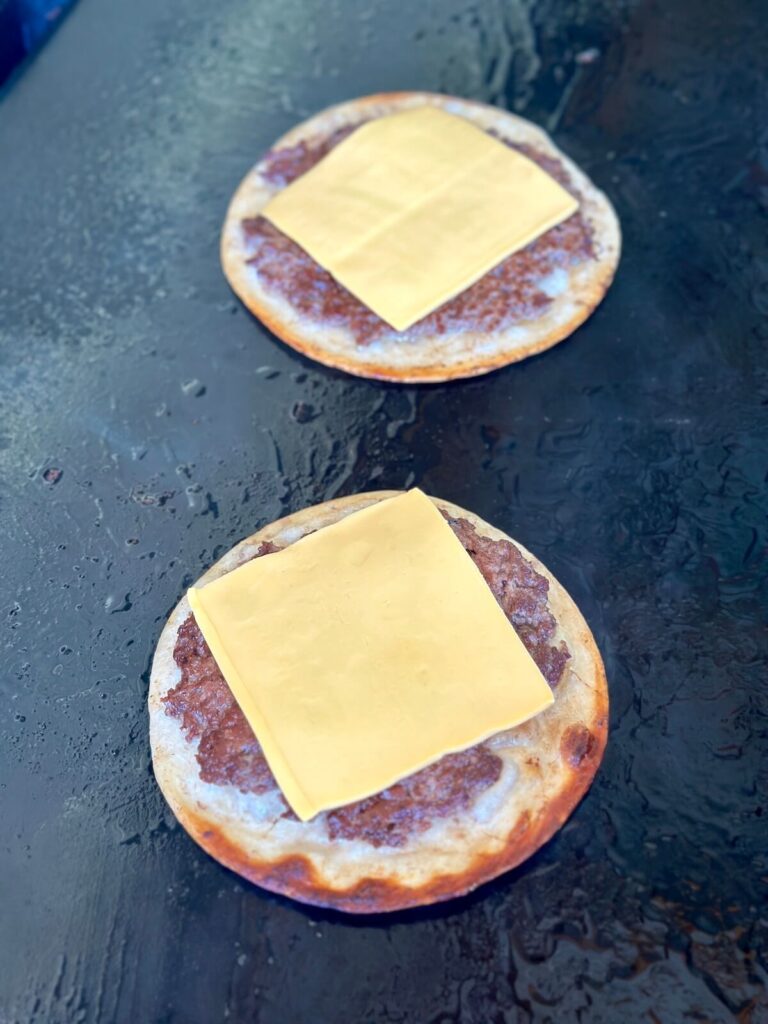 cooking smashed tacos with American cheese on a griddle