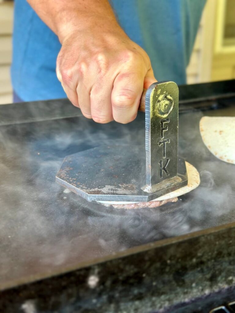 using a burger press to make smash burger tacos on a Blackstone griddle