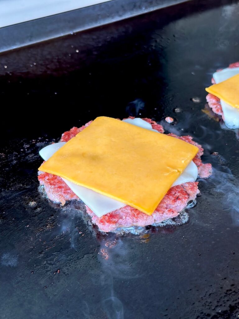 sausage patty cooking on a griddle with sliced cheese