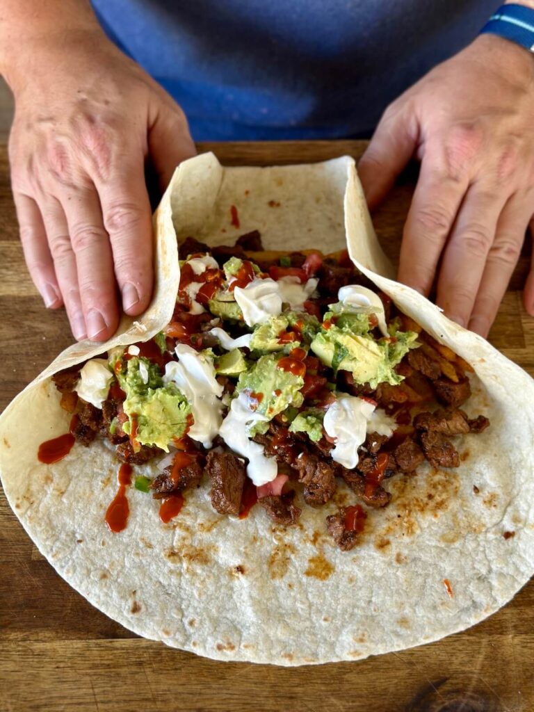 rolling up a California burrito with steak, french fries, guacamole, and sour cream