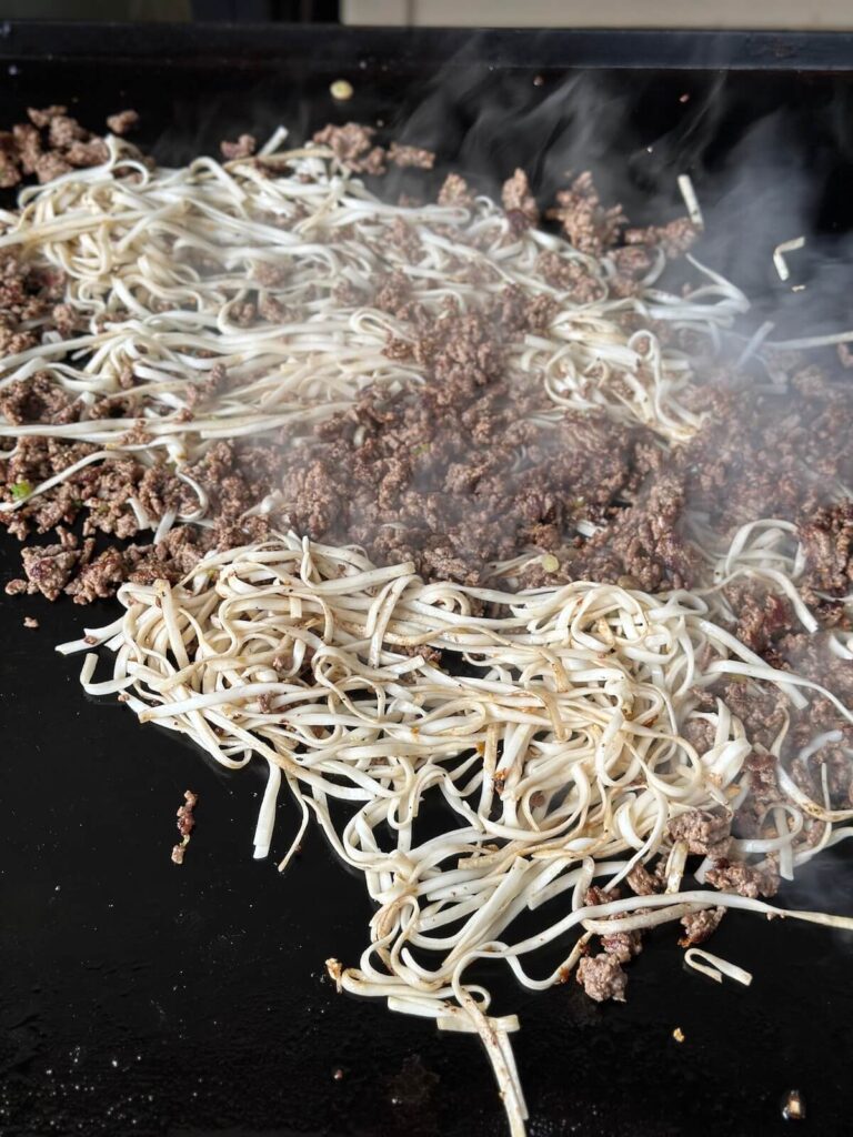 cooking Mongolian noodles with ground beef on a griddle