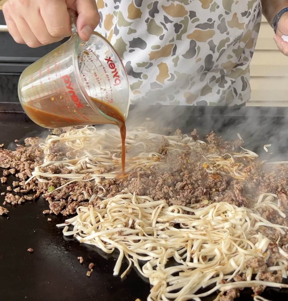 pouring Mongolian sauce onto noodles and ground beef