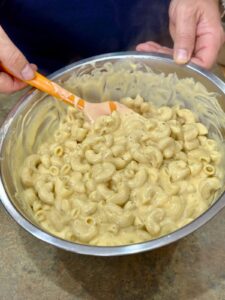 mixing cheese sauce and macaroni noodles in a mixing bowl
