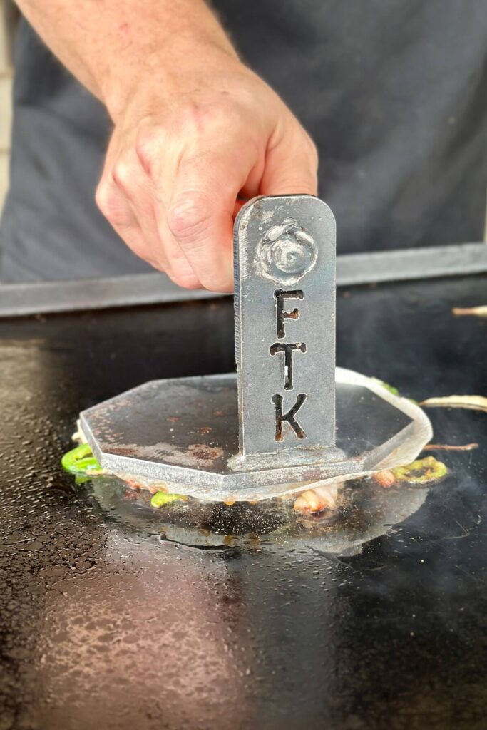 using a burger press to smash jalapeno smash burgers on a griddle
