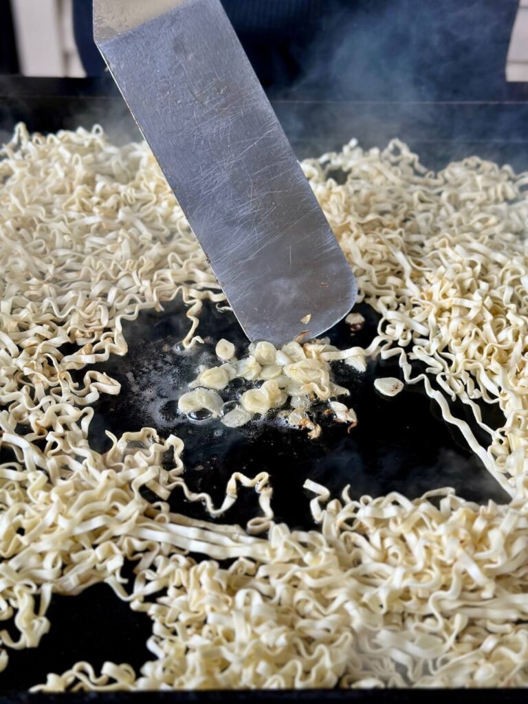 sautéing garlic in butter on a griddle with noodles