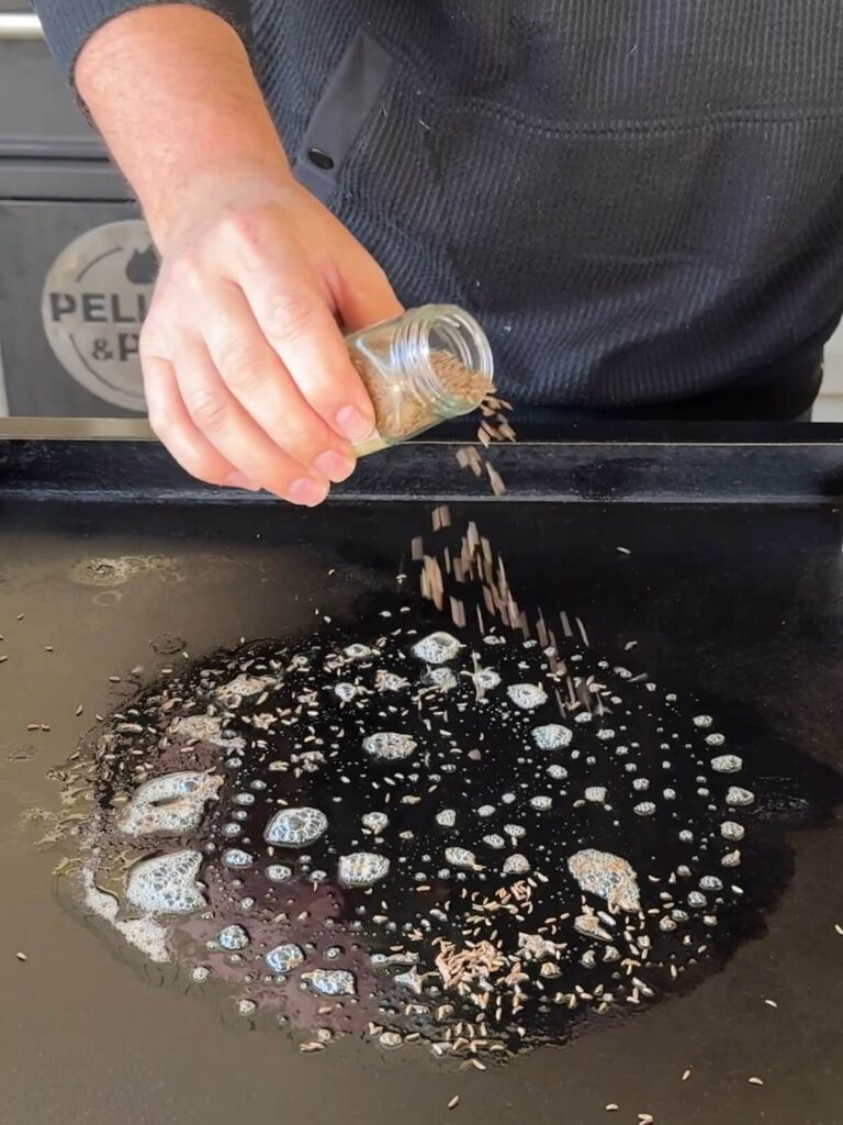 sprinkling caraway seeds into melted butter on a griddle