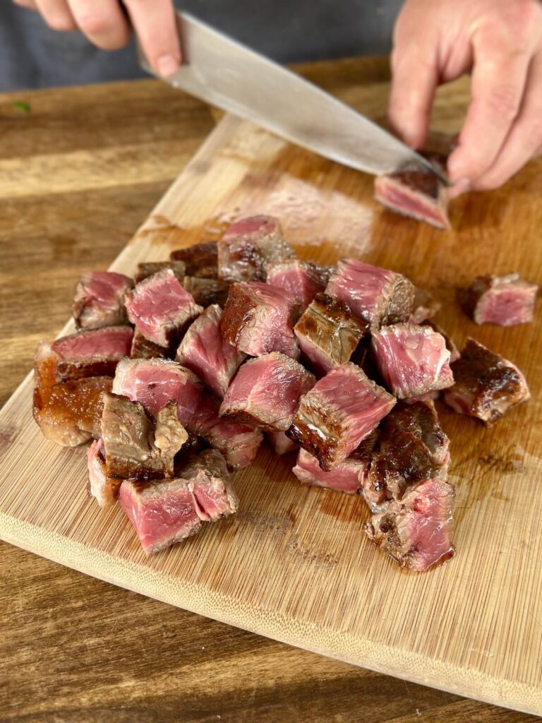 cutting seared steak into bite-sized cubes
