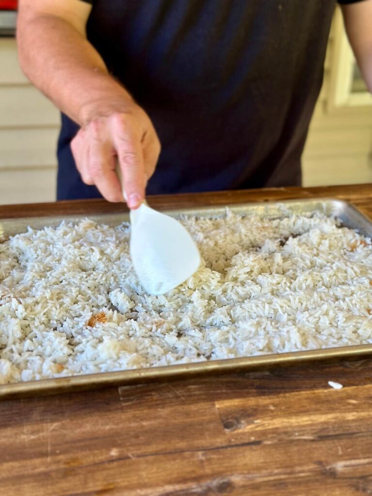 spreading cooked coconut rice out on a sheet tray