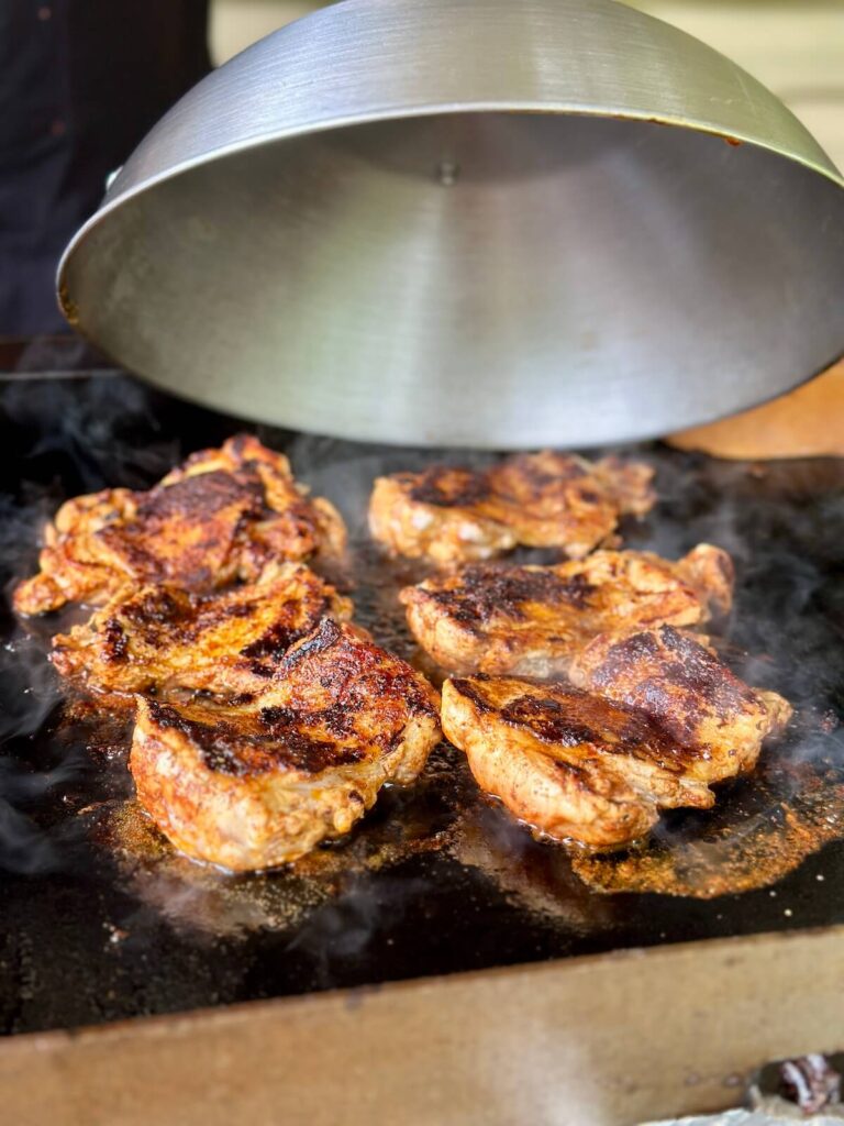 covering chicken with a dome as it cooks on a griddle