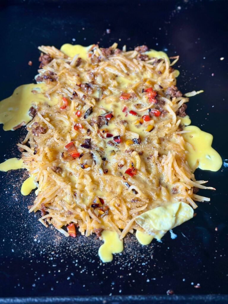 shredded hash brown potatoes cooking with eggs, chorizo, and sautéed vegetables