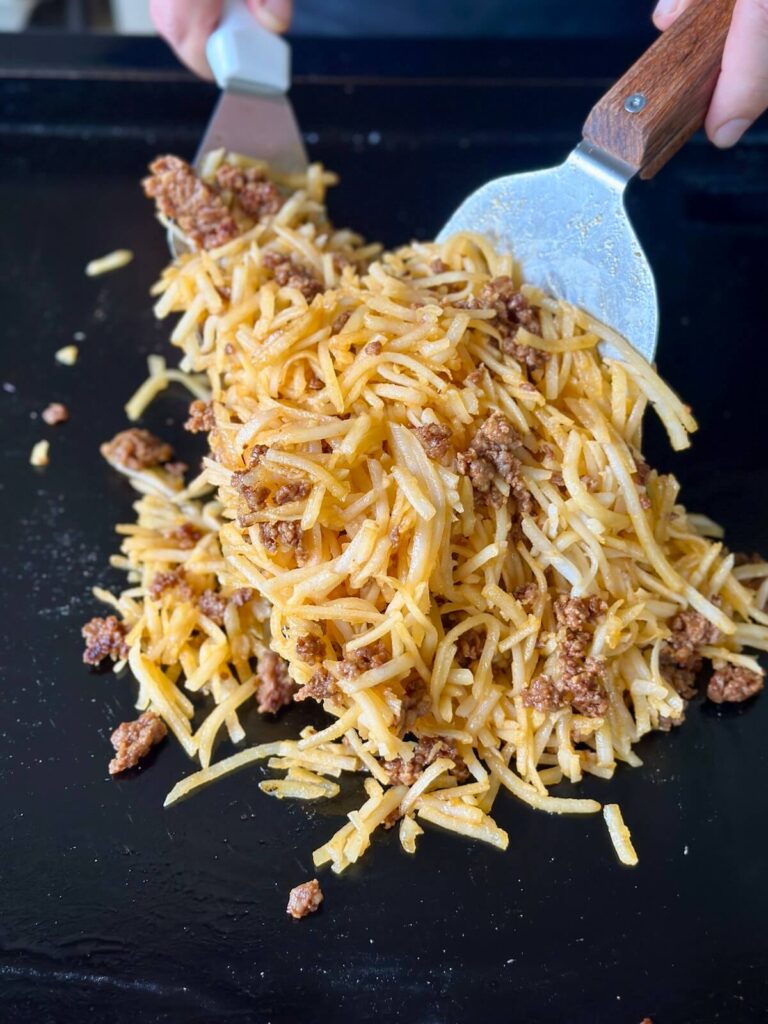 mixing shredded hash browns and chorizo on a griddle