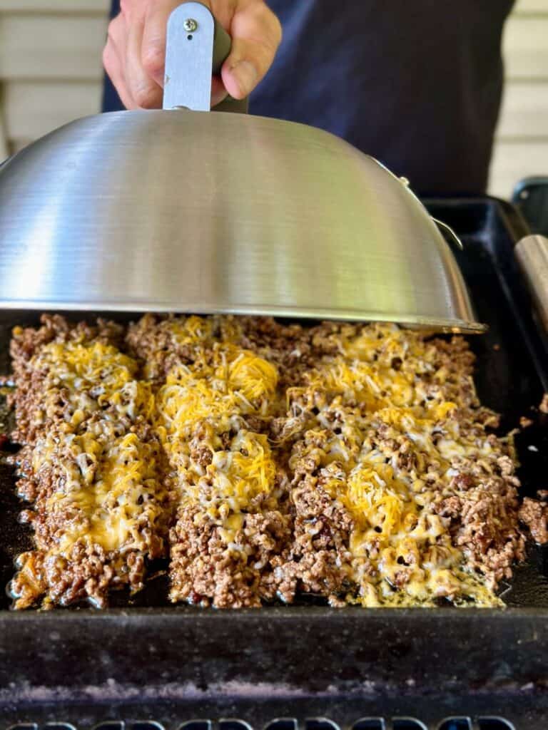 using a melting dome to melt cheese on taco meat on a griddle