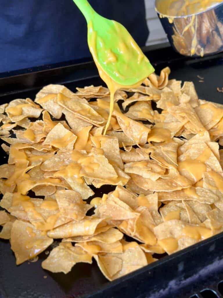 spooning nacho cheese on tortilla chips on a griddle