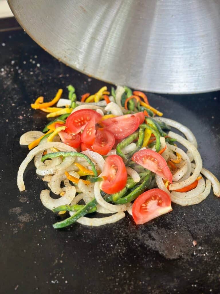 sautéing sliced bell peppers, onions, and tomatoes on a griddle
