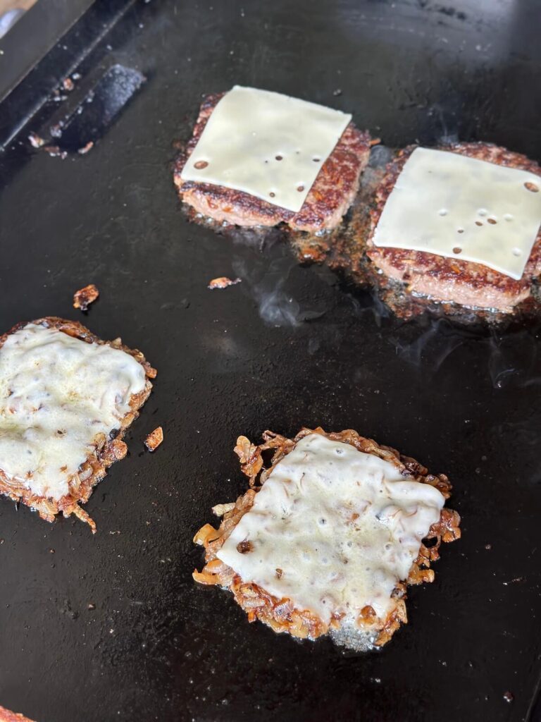 french onion burger patties with Swiss cheese cooking on a griddle