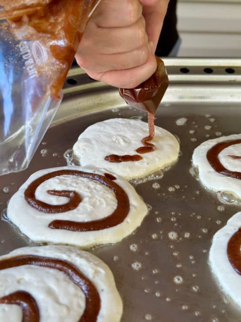 piping cinnamon and sugar filling in a circle on top of pancakes cooking on a griddle