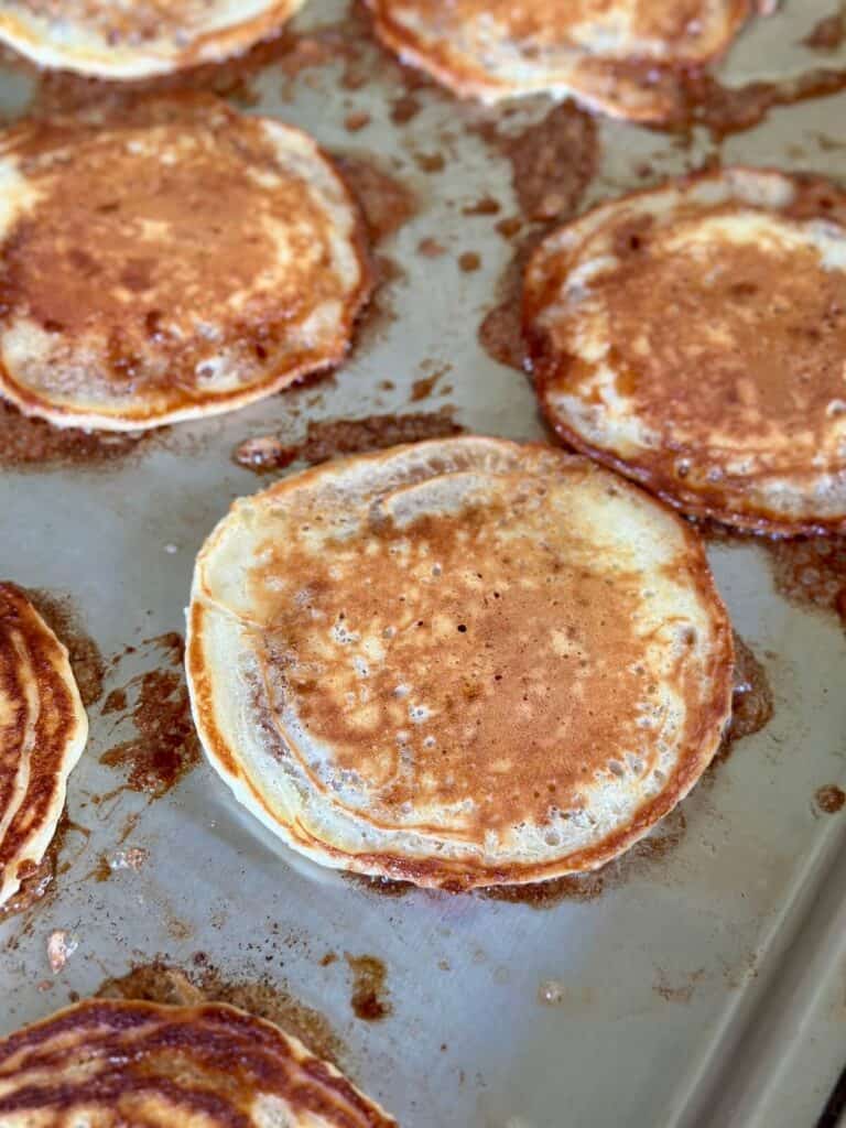 cooking cinnamon roll pancakes on a griddle