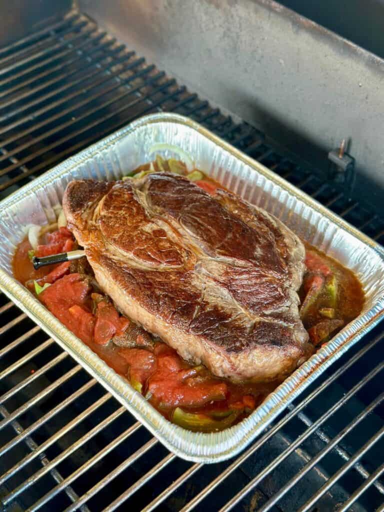 braising a chuck roast in a foil pan with peppers and onions