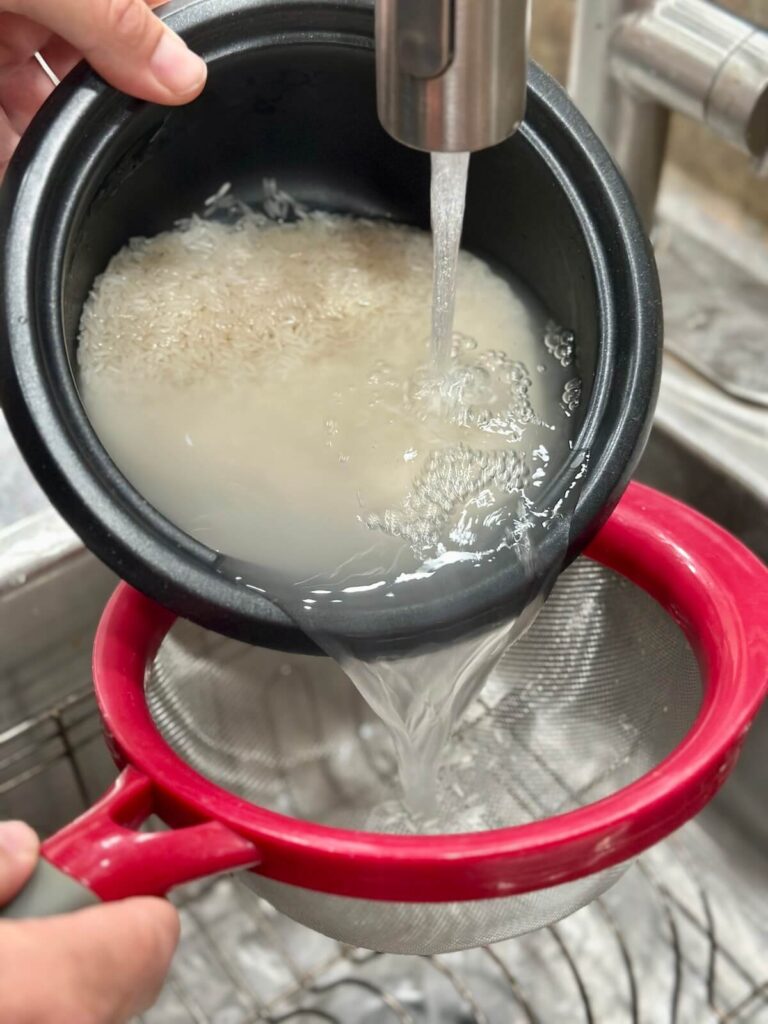 rinsing white rice under running water in a sink